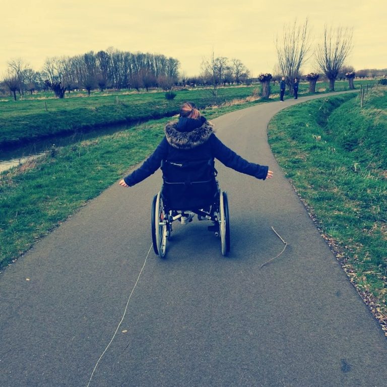 Cindy gaat op pad. Cindy rijdt in haar rolstoel in het buitengebied.